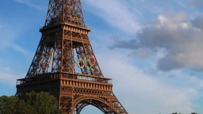 Eiffelturm mit olympischen Ringen vor blauem Himmel und Wolken: Symbol für die Olympischen Spiele in Paris 2024 und internationales Projektmanagement.