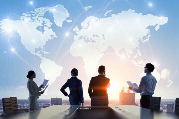 Vier Geschäftsleute in einem Meeting, im Hintergrund eine Weltkarte: Symbol für internationales Projektmanagement und globale Zusammenarbeit.