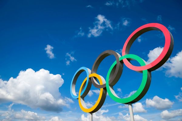 Große olympische Ringe vor blauem Himmel mit weißen Wolken: Symbol für internationale Zusammenarbeit und Projektmanagement bei den Olympischen Spielen.