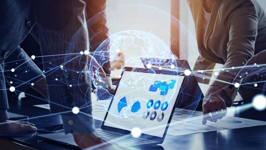 Laptop mit Daten-Dashboard auf einem Konferenztisch, umgeben von Geschäftsleuten, die Dokumente prüfen. Im Vordergrund ist eine digitale Weltkugel mit vernetzten Linien eingeblendet, Symbol für IT-Governance, globale Vernetzung und Datenanalyse. 