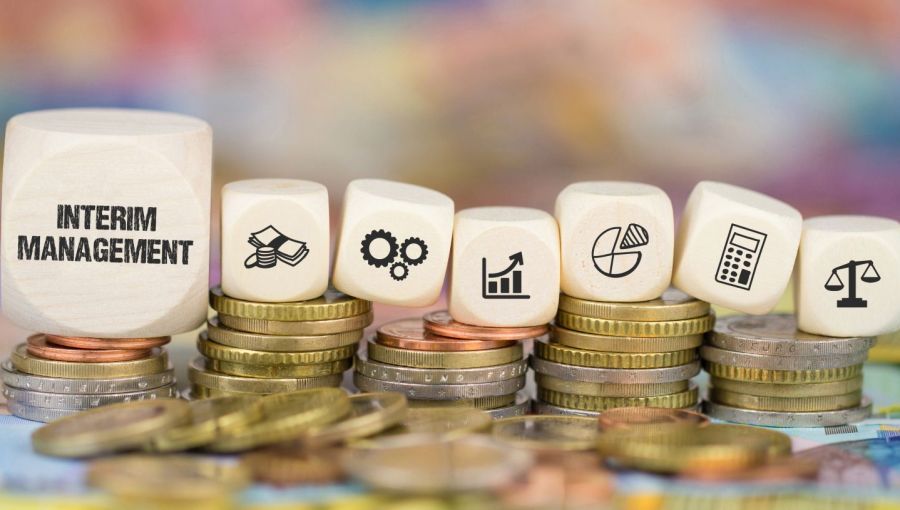 Holzwürfel mit Symbolen zu Finanzen, Prozessen und Kennzahlen stehen auf gestapelten Münzen: Visualisierung des ROI von Interim Management im Unternehmen. 