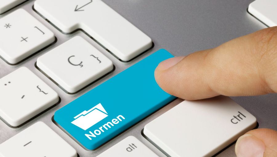 Finger tippt auf blaue Taste „Normen“ auf Computertastatur als Symbol für Standards und Richtlinien im Projektmanagement. 