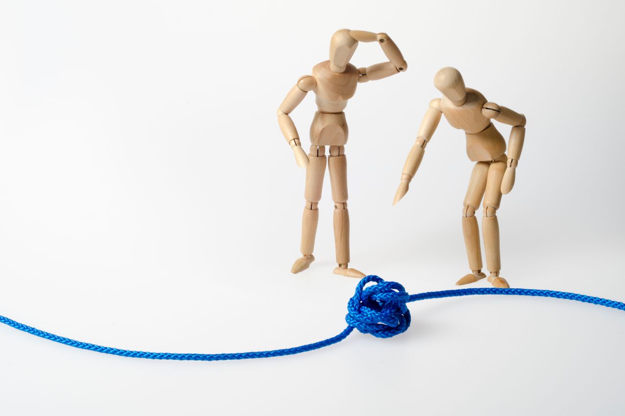 Zwei Holzfiguren betrachten einen Knoten – steht für komplexe Konflikte und gemeinsame Lösungsfindung.